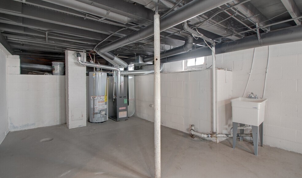 Full unfinished basement with painted concrete floors and utility equipment